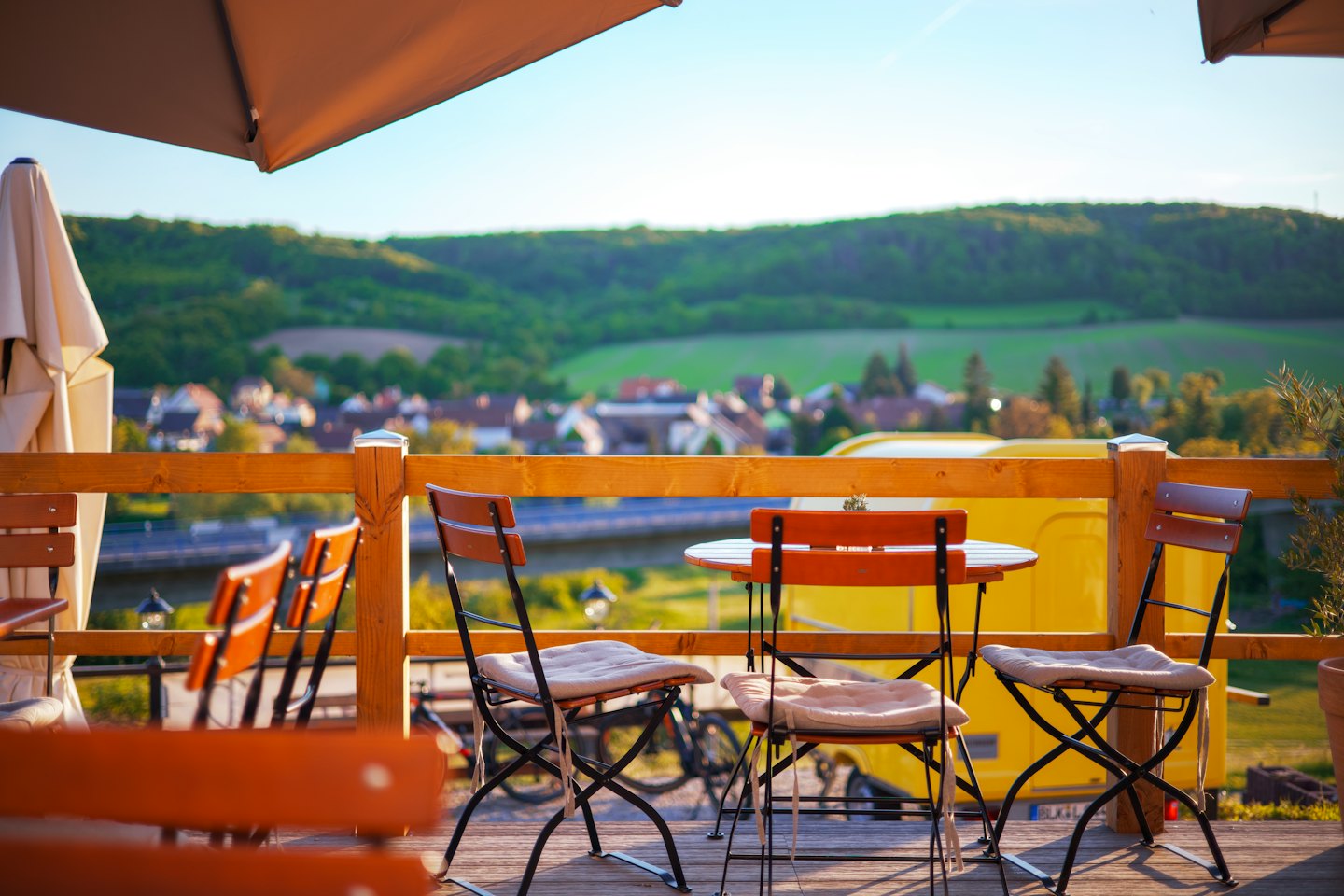 Tables vides sur la terrasse d'un café, avec vue sur une vallée verdoyante.