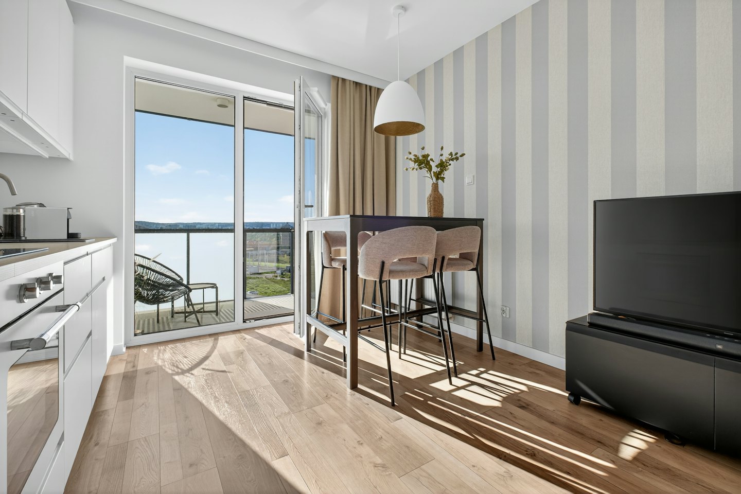Intérieur d'appartement moderne avec cuisine, coin repas et vue sur le balcon.