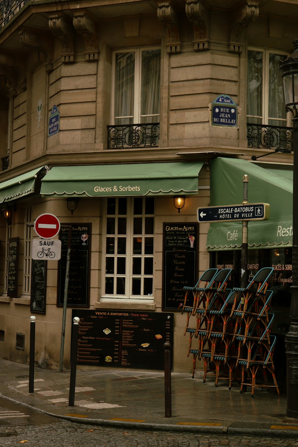 Coin de rue parisien avec auvents verts et chaises d'extérieur empilées.